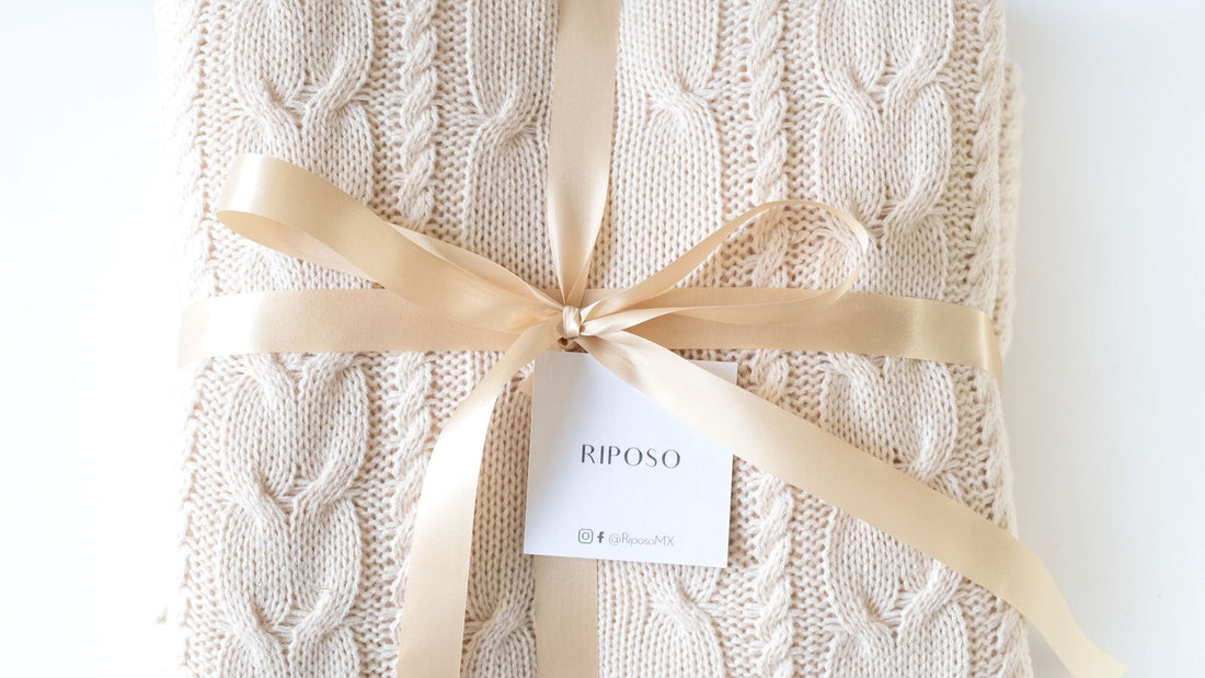 Frazada tejida beige de Riposo envuelta con listón dorado, hecha en México